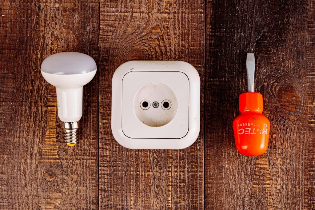 Light bulb, wall socket and screwdriver laid out on a workbench